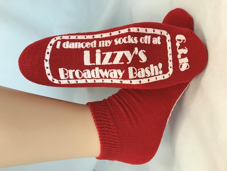 Puede incluir: Calcetines rojos hasta el tobillo con un dise&ntilde;o blanco en forma de boleto que dice "I danced my socks off at Lizzy's Broadway Bash!" y "Oct. 16".
