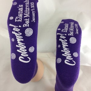 May include: Purple socks with white text that reads "Celebrate! Elena's Bat Mitzvah January 5, 2013".