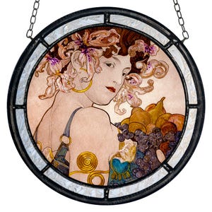 May include: Round stained glass panel featuring a woman with floral hair and gold jewelry, holding a basket of fruit. The artwork is framed in black with a white and iridescent border, and is suspended by a chain.