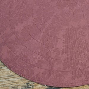 May include: A round, pink placemat with a floral pattern. The pattern is a series of concentric circles with a floral design.