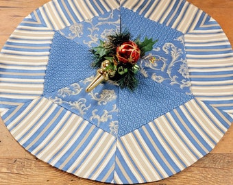 May include: A blue and beige striped Christmas tree skirt with a patterned center. The skirt is made of fabric and has a scalloped edge.