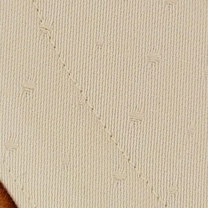 May include: Close-up of a beige fabric with a subtle diamond pattern. The fabric has a smooth texture and a slightly textured surface.