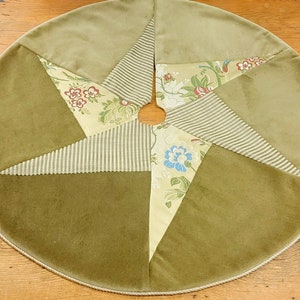 May include: A green velvet Christmas tree skirt with a star design. The skirt is made of different fabrics, including striped and floral patterns.