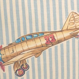 May include: A vintage-style illustration of a brown airplane with a red number 33 on the side. The airplane is flying over a blue and white striped background. The airplane has a blue propeller and a white tail with the text "IK 170" on it.