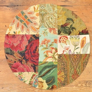 May include: A round patchwork table runner featuring a variety of floral and paisley patterns in shades of red, green, blue, and brown.