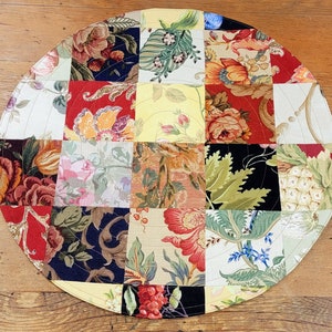 May include: A round patchwork table runner with a floral design. The runner is made of different fabrics in shades of red, green, yellow, and white. The runner is approximately 30 inches in diameter.