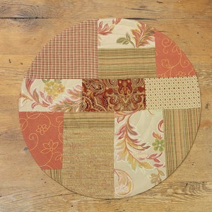 May include: Round patchwork table runner with a variety of floral and geometric patterns in shades of brown, beige, and orange.