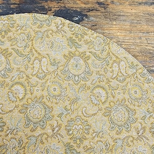 May include: A close-up of a fabric with a gold and silver floral pattern. The fabric has a textured, woven look.