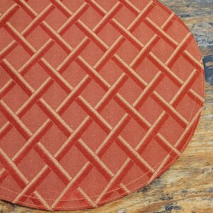 May include: A round, orange placemat with a woven pattern of thin, light orange lines. The placemat has a stitched edge.