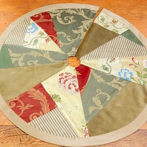 May include: A round, beige-trimmed Christmas tree skirt with a patchwork design. The skirt is made of various fabrics with floral patterns in shades of green, red, and beige.