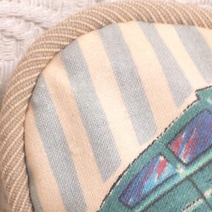 May include: A beige and blue striped fabric eye mask with a green and blue airplane design. The eye mask has a beige trim around the edges.