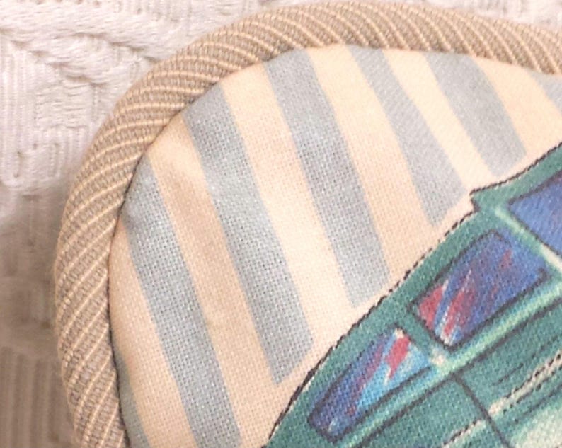 May include: A beige and blue striped fabric eye mask with a green and blue airplane design. The eye mask has a beige trim around the edges.
