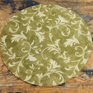 May include: A round green placemat with a white floral pattern. The placemat is made of a textured fabric.