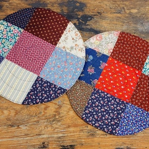 May include: Two round patchwork placemats featuring a variety of floral and geometric patterns in shades of red, blue, brown, and white.