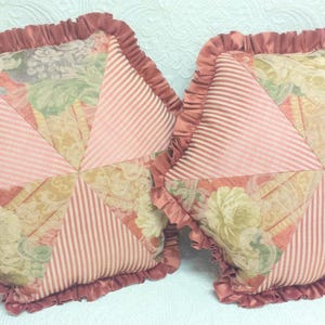 May include: Two decorative throw pillows with a pink and white striped fabric and a floral pattern. The pillows have a ruffled edge.