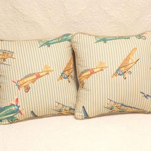 May include: Two decorative throw pillows with a blue and white striped background and a pattern of vintage airplanes in shades of blue, green, red, and yellow.
