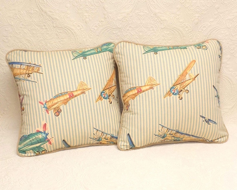 May include: Two decorative throw pillows with a blue and white striped background and a pattern of vintage airplanes in shades of blue, green, red, and yellow.