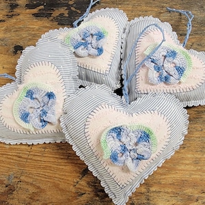 May include: Five blue and white striped fabric heart-shaped ornaments with pink and green crocheted flowers in the center.