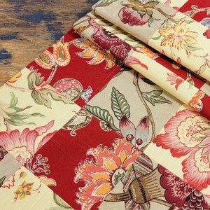 May include: A patchwork table runner with a floral design in shades of red, yellow, and beige. The runner is made of fabric and has a quilted texture.