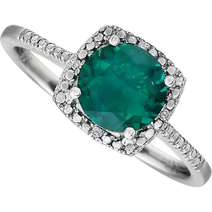 May include: A silver ring with a large, emerald green gemstone surrounded by a halo of smaller diamonds. The band is also set with smaller diamonds.