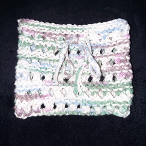 May include: A white knitted dishcloth with a green, blue, and pink striped pattern. The dishcloth has a fringe on one side.