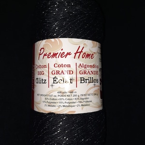 May include: A black yarn ball with silver metallic thread. The label reads "Premier Home" and lists the yarn content as 83% cotton, 15% polyester, and 2% metallic. The yarn is 490 yards and weighs 9.87 ounces.