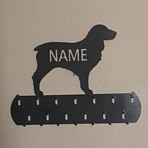 May include: Black metal dog silhouette wall hook with the word "NAME" in white lettering. The hook has 10 metal hooks on the bottom for hanging items.