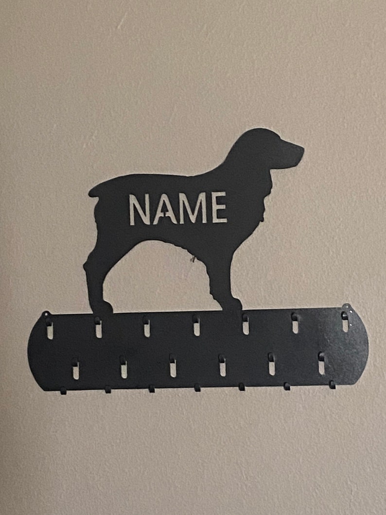 May include: Black metal dog silhouette wall hook with the word "NAME" in white lettering. The hook has 10 metal hooks on the bottom for hanging items.
