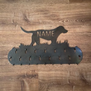 May include: Metal dog silhouette key holder with the word "NAME" engraved on the dog's body. The holder has 20 hooks for hanging keys, leashes, or other items.