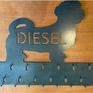 May include: Metal key holder shaped like a dog silhouette with the name "Diesel" cut out. The holder has 15 hooks for hanging keys.