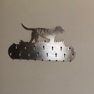 May include: Metal dog silhouette key holder with the word "NAME" in the center. The holder has 20 hooks for hanging keys.