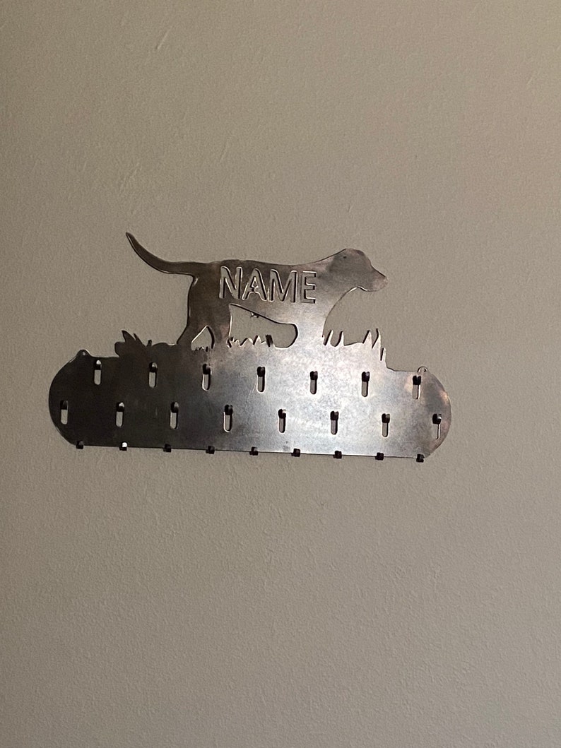 May include: Metal dog silhouette key holder with the word "NAME" in the center. The holder has 20 hooks for hanging keys.
