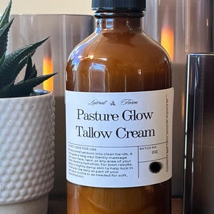 May include: A brown glass bottle with a black pump top and a white label that reads "Pasture Glow Tallow Cream". The label also includes directions for use and a batch number of 002.