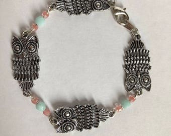 May include: A silver bracelet with three owl charms and light blue and pink beads.