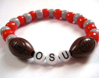 May include: A red and gray beaded bracelet with two brown football charms and white letter beads spelling "OSU".