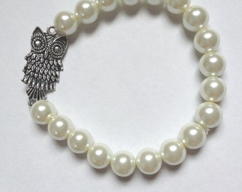 May include: A white pearl bracelet with an owl charm. The owl is silver and has detailed features.