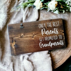 May include: A wooden sign with the text "Only the best parents get promoted to grandparents" in white lettering. The sign has a rustic brown finish and a metal clip at the top.