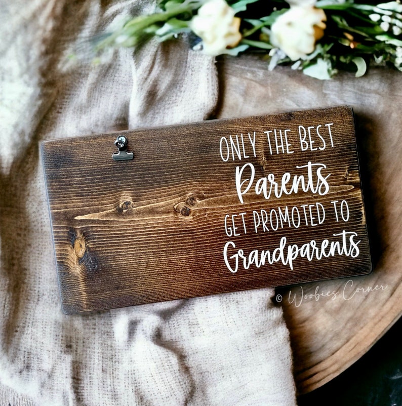May include: A wooden sign with the text "Only the best parents get promoted to grandparents" in white lettering. The sign has a rustic brown finish and a metal clip at the top.