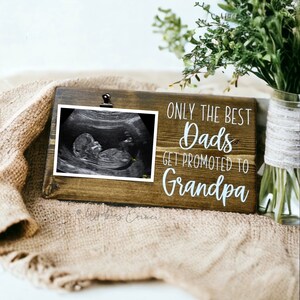 May include: A wooden sign with a photo clip holding an ultrasound image. The sign reads "Only the best dads get promoted to grandpa".
