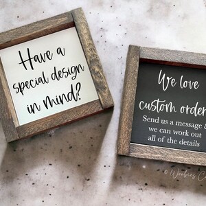 May include: Two wooden signs with a rustic finish. The sign on the left says "Have a special design in mind?" The sign on the right says "We love custom orders! Send us a message & we can work out all of the details." The signs are on a gray background.