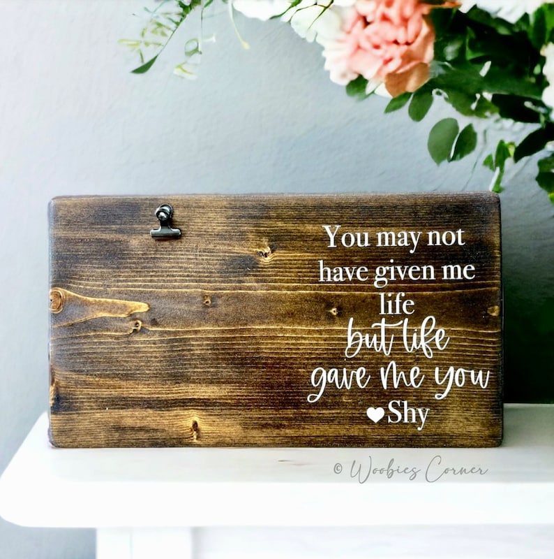 May include: A dark brown wooden sign with a clip at the top. The sign has white text that reads "You may not have given me life but life gave me you Shy".