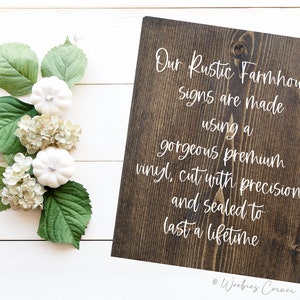 May include: A dark brown wooden sign with white text that reads "Our Rustic Farmhouse Signs are made using a gorgeous premium vinyl, cut with precision and sealed to last a lifetime." The sign is on a white wood background.
