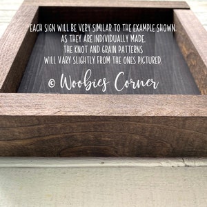 May include: A dark brown wooden frame with a black sign inside. The sign has white text that reads: "EACH SIGN WILL BE VERY SIMILAR TO THE EXAMPLE SHOWN. AS THEY ARE INDIVIDUALLY MADE. THE KNOT AND GRAIN PATTERNS WILL VARY SLIGHTLY FROM THE ONES PICTURED. &copy; Woobies Corner"