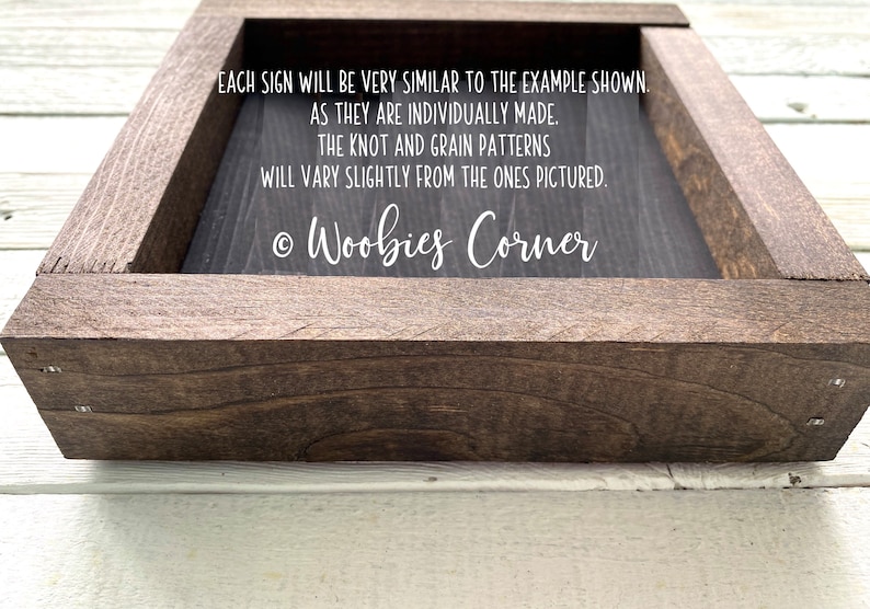 May include: A dark brown wooden frame with a black sign inside. The sign has white text that reads: "EACH SIGN WILL BE VERY SIMILAR TO THE EXAMPLE SHOWN. AS THEY ARE INDIVIDUALLY MADE. THE KNOT AND GRAIN PATTERNS WILL VARY SLIGHTLY FROM THE ONES PICTURED. &copy; Woobies Corner"