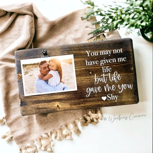 May include: A wooden photo frame with a clip to hold a photo. The frame has a white inscription that reads "You may not have given me life but life gave me you Shy".