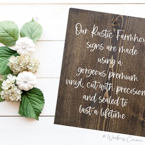 May include: A dark brown wooden sign with white text that reads "Our Rustic Farmhouse Signs are made using a gorgeous premium vinyl, cut with precision and sealed to last a lifetime." The sign is on a white wood background.