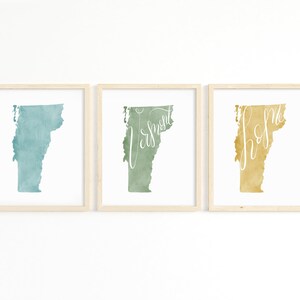 May include: Set of three framed art prints featuring the state of Vermont. Each print showcases a watercolor-style map of Vermont in shades of teal, green, and gold, with the words "Vermont" and "home" in cursive.