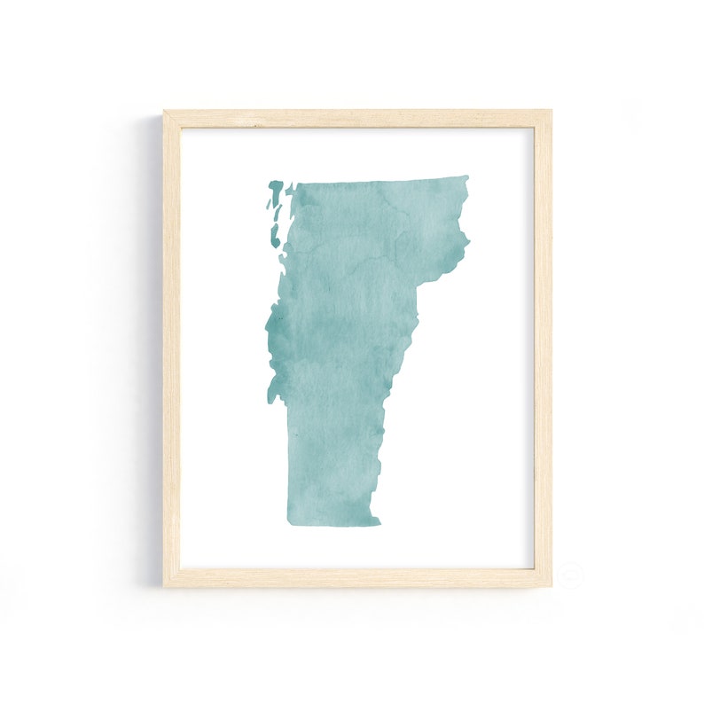 May include: A framed print featuring a teal watercolor map of Vermont. The map is centered on a white background, enclosed within a light wood-colored frame. The artwork has a minimalist aesthetic.