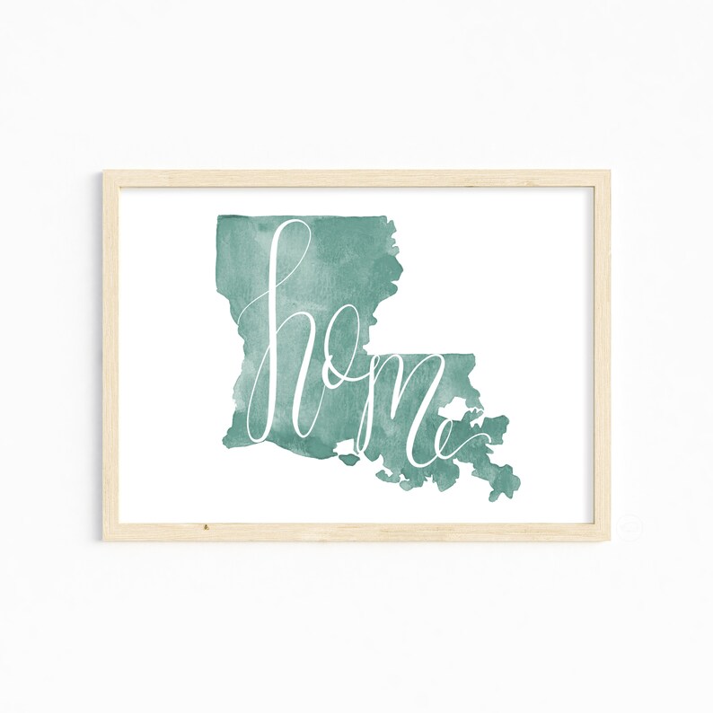 May include: A framed watercolor print featuring the state of Louisiana in teal with the word "home" in white script. The artwork is set against a white background, encased in a light wood frame.