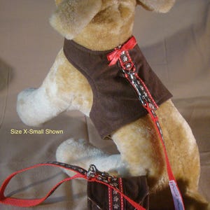 May include: A brown dog harness and lead set with red detailing. The harness is a vest style, and the lead and harness feature a paw print pattern. A small matching bag is also included in the set.